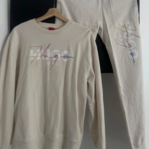 Beige mjukisbyxor från Hugo - Snyggt beige mjukisset från Hugo med färgglatt tryck på benet & bröstet. Perfekta för en avslappnad stil med elastiska muddar vid bensluten.