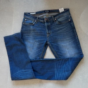 Blå slim fit jeans från Jack&Jones - Snygga blå slim fit jeans med klassisk femficksdesign. Jeansen har en medelblå tvätt och är perfekta för en stilren look. De har en knappgylf och är tillverkade i ett slitstarkt denimtyg. Storlek 31/34