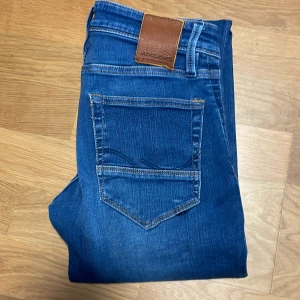 Blå jeans från Jack & Jones - Snygga blå jeans från Jack & Jones med klassisk femficksdesign och läderpatch på baksidan. Perfekta för en avslappnad stil.