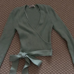 Grön ribbad omlottopp  - Snygg grön ribbad omlottopp  med långa ärmar och knytband i midjan. Perfekt för en stilren look.