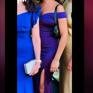 Lila axelbandslös klänning - Jättefin lila klänning i satin med offshoulder-design och en elegant slits framtill. Perfekt för bal eller festlig kväll! Klänningen har en figurnära passform. Storlek XS men passar S med 😊🩷