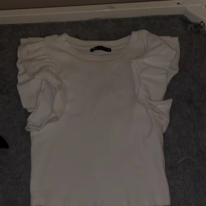 Fin kort tröja med puffade/volanger på armarna - En vit lite kortare t-shirt med volanger på armarna, fin att ha på fest eller bara en vardag ☺️ 