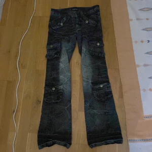 Svarta low rise bootcut jeans - Säljer ett par japanska cargo-jeans i storlek 28/29, de är bootcut med en low rise och har massa snygga detaljer Midja: 76cm Rise: 22.5 cm Längd: 101cm Benöppning: 23cm
