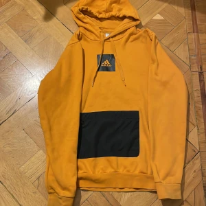 Gul/Orange adidas tjocktröja hoodie - Begagnad Adidas hoodie. Ficka på magen. Snören finns kvar. Bra skick, använd ett par gånger. 