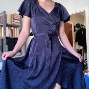 Prickig vintageklänning - Jättefin mörkblå klänning från Stockholms Klänningsfabrik. Har orangea prickar på. Det är en omlottklänning, så man kan till viss del justera storleken. Köpt second hand men bara använd en gång av mig