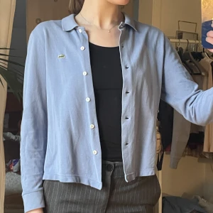 Lacoste Kofta - Ljusblå kofta från Lacoste. Finns tecken på användning och en vag fläck (se bild 3). Sitter som S.