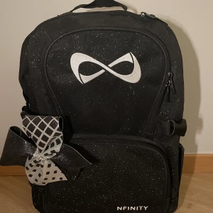 Cheerleading ryggsäck  - Svart Nfinity sparkle ryggsäck med vitt Nfinity märke. Mått:  Bredd 29 cm  Höjd 45 cm  Djup 25 cm Glitter rosett i silver och guld ingår:)  Köparen står för frakten