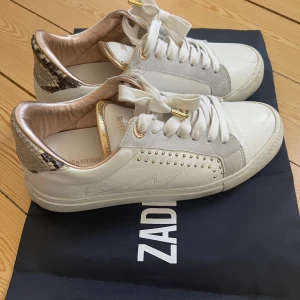Zadig sneakers storlek 39 - Supersnygga vita sneakers från Zadig. Grå detalj i mocka och guldnitar på sidan. Animal print på hälen. Använda fåtal gånger och säljer pga köpt fel storlek. Inköpta i butiken på Birger Jarlsgatan i Stockholm för några år sedan. Nypris 2.250 kronor.