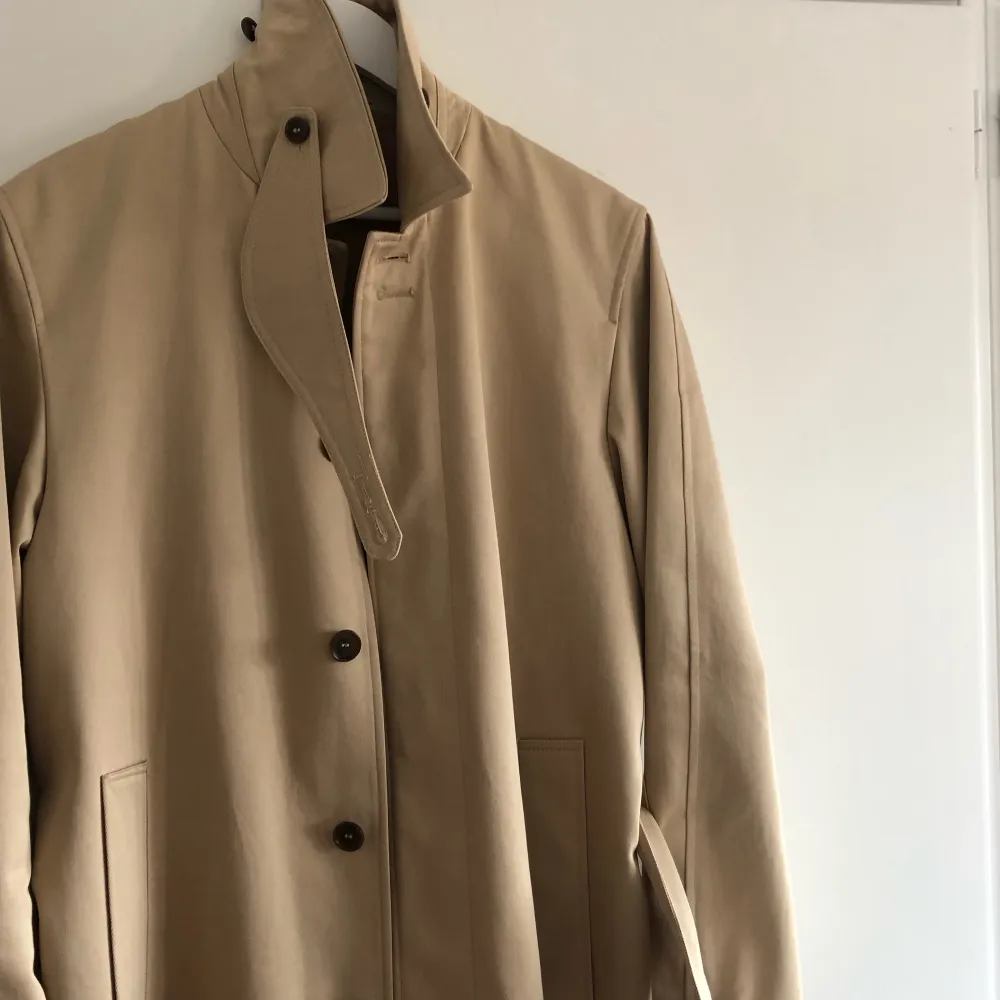 Trenchcoat i klassisk rak passform med bälte i midjan. Rocken ner till knäna om man är runt 175 cm lång. Rocken är även vattenavvisande . Jackor.