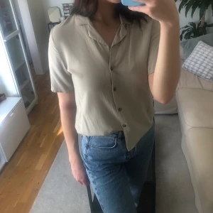 Beige skjorta från Gina Tricot - Beige jätteskön viskos skjorta med korta ärmar från Gina Tricot. Storlek 38. Går att syla på olika sätt. Använt skick. Extraknapp finns med.
