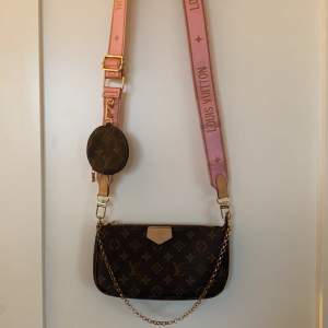 En brun lv väska med rosa band med guld kedja. Säljer för 700 kr. Nästan aldrig använt den .