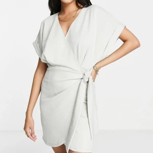 ASOS Design - ljusgrå omlottklänning i storlek EU40 - Ljusgrå texturerad mini-omlottklänning med korta ärmar. Skön och snygg klänning i nytt skick, oanvänd! Stretchigt material. Säljer den då den inte kommer komma till användning och returtiden har passerats