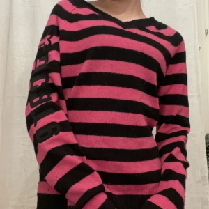 Randig stickad tröja - Rosa och svartrandiga stickad tröja med broderad text på armen. Inga defekter💗