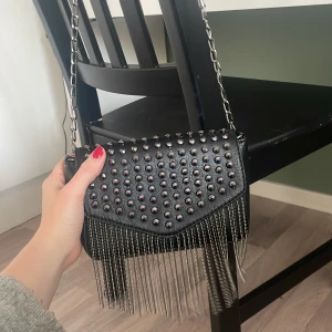 Väska med nitar! - Hej säljer denna så fina väska med nitar och tassel. Bra storlek, blandning liten och mellan storlek!. Helt ny och aldrig använd, INGA som helst skador på väskan och det finns ett litet fack inuti!