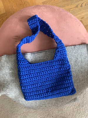 Kornblå virkad väska - Hej! Säljer en kornblå handvirkad axelremsväska. Väskan mäter ca 34 x 24 cm i storlek med en axelrem på ca 80 cm. Sitter snyggt cross body, se bild!