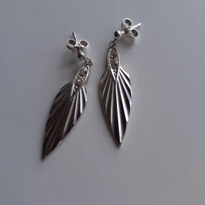 Silverörhängen  - Örhängen i äkta silver formade som vingar. Supersöta med gravering  och med 2 stenar i vadera hönge. Helt oanvända och i nyskick, silverfärg en är lite ljusare än vad som ljuset visar på bilden. Har 3 exemplar och säljer dem för 250 kr/st. Storlek: 3 × 1 cm