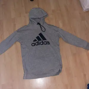Adidas gråa träningshoodie med svart text och svarta snören. Passform till en man. Tjock hoodie och oversize på en kvinna. Original pris 529kr