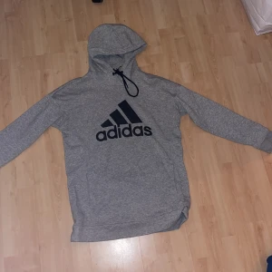 Adidas gråa träningshoodie med svart adidas text, svarta snören.  - Adidas gråa träningshoodie med svart text och svarta snören. Passform till en man. Tjock hoodie och oversize på en kvinna. Original pris 529kr