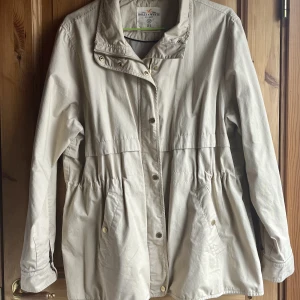 Trenchcoat-Lindex - En näst intill oanvänd trenchcoat från Lindex med snyggt fall. Säljs ej längre. Har dold snörning vid midjan som man kan anpassa efter egen storlek. 