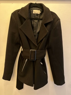 Svart kappa - svart kappa från NLY trend. Inköpt för 699kr och säljer den för 450kr. Varan är slutsåld på Nelly!  Kappan har fina silverdetaljer och ett skärp i midjan Har använt den max 2 gånger men känner att den inte riktigt är min stil! Storlek M (passar S & L) 