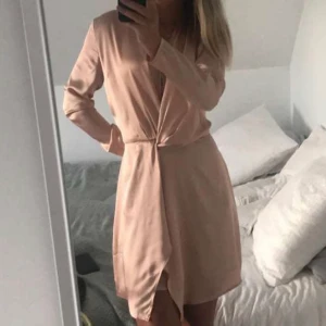 Ljusrosa miniklänning - Långärmad ljusrosa miniklänning i satinliknande material. Dragkedja i ryggen