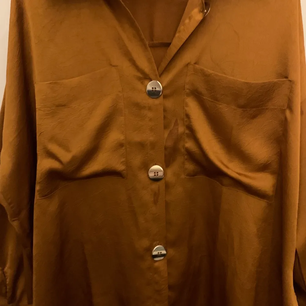 Orange oversized skjorta/blus från GinaTricot med ”guldiga”/mässings knappar! Med mönstrade detaljer i tyget. Den är dessvärre lite fläckig!. Blusar.