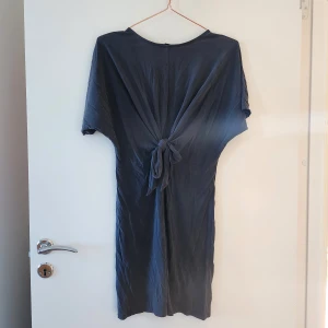 Grå t-shirtklänning - Supersnygg t-shirtklänning med knytdetalj i midjan, vilket gör att överdelen är lite mer som en t-shirt men du får markerad midja och supersnygg, lite tightare kjol. Säljer pga för liten. Hör av dig om du har frågor!