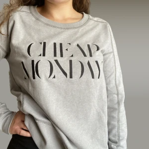 Sweatshirt Cheap Monday - Grå sweatshirt från Cheap Monday med svart broderat tryck. Använd några gånger men i fint skick. Tröjan har en ”sliten” look med tydlig och lite ”grov” söm. Sitter lite oversize på mig som normalt är mellan S och M. Nypris 499:-