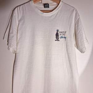 En fantastiskt fin Stussy t-shirt från sent 80-tal/tidigt 90-tal. I jättefint skick med tanke på att den är över 30 år gammal. Lätt fading på trycket och en intvättad känsla i tyget. Benvit färg. Single stitching på ärmar och midjeöppning. All USA made. 