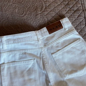 Vita jeans NAKD - Jag säljer dessa högmidjade vita jeans från NAKD. Använda en gång, storlek 32, passformen är rak men lite bredare ner mot benen.