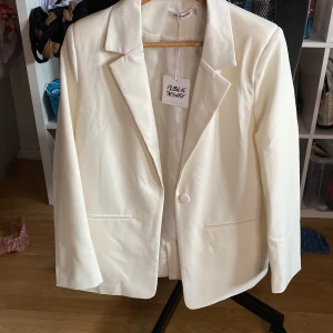 En vit blazer som är helt oanvänd  - En vit blazer från Nelly som är helt oanvänd, köpte av en annan tjej här på Plick men den var liten för mig därav säljer jag den. 