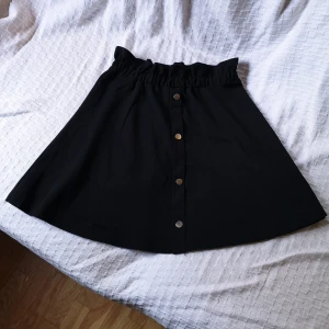 kjol strl S - Enkel svart kjol, resår i midjan. Är storlek S. Knapparna är i silver och bara dekorativa. 