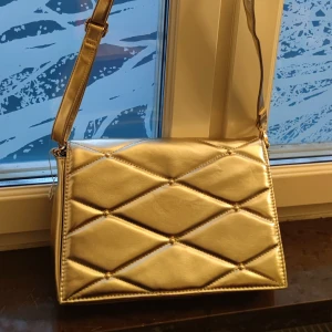 Guldig helt ny handväska  - En guldig ganska rymlig handväskan med band och kedja. Ficka inuti. Helt oanvänd, brand new! 