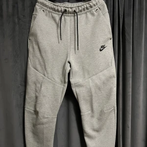 Nike Tech - Gråa Nike Tech byxor med svarta detaljer. Byxorna är testade men har aldrig använts ute så dem är precis som nya, väldigt bra och fint skick. Storlek S. Pris kan diskuteras. Köparen står för frakten. Betalning via Swish.