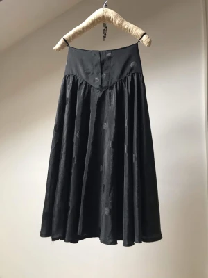 Svart kjol - Svart KJOL i polyester med kvarta prickar som mönster. Elastisk baksida på midjan. Kjolen blir vid först efter ett V format liv framtill- som ger en väldigt smickrande passform.  Storlek  XS/S Pris 250 kr  Midja från 62- 76 cm Längd 79 cm