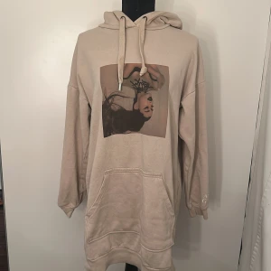 Ariana grande lång hoddie - En längre ariana grande hoddie med tryck på magen och på vänster arm. 