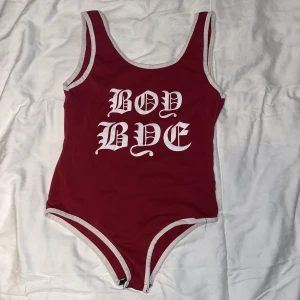 Röd body - Röd body med text och vit inramning. Står ingen storlek men gissar på XS/S. 