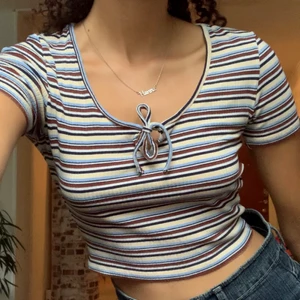 Randig Topp - Randig i brunt, blått, gult, vitt & svart.  Storlek XS men jag själv bär oftast S eller M. Sparsamt använd! Stretchig! Har två snören framtill som kan knytas till en rosett.  Möts upp eller fraktar, köparen betalar frakt. Ansvarar inte för postens slarv. 