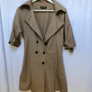 Kortärmad beige/khaki kappa med bruna stora knapar för vår väder eller kyligare sommar väder. Jättefin och klassig. Knä lång