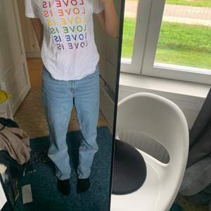 En vit T-shirt med texten love is love i rengnbågens färger. 