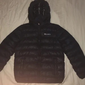 Mörkblå Champion Hooded Jacka - Storlek 164 Är i bra skick förutom under armhålan där det är ett litet hål som inte syns och inte släpper in kyla. Den är ungefär 1 år gammal och användes från jul till sen Mars 2021-2022. Den passar väldigt bra för folk som är 1,58 till 1,64