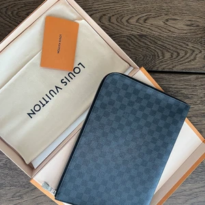 Louis Vuitton pochette jour GM  - Louis Vuitton pochette jour GM i nyskick, inga spår efter användning. Använt den ca 2 gånger. Passar till papper eller dator fordral för MacBook ca 15/16 tum. Jag hade den till en 13 tum vilket också funkar. Nypris 7600kr 