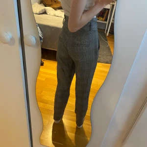 Rutiga kostymbyxor storlek XS - Grå rutiga kostymbyxor i fint skick, säljer då de inte kommer till användning. Ganska korta i längden, och anpassningsbar i midjan. Ganska stora framfickor.