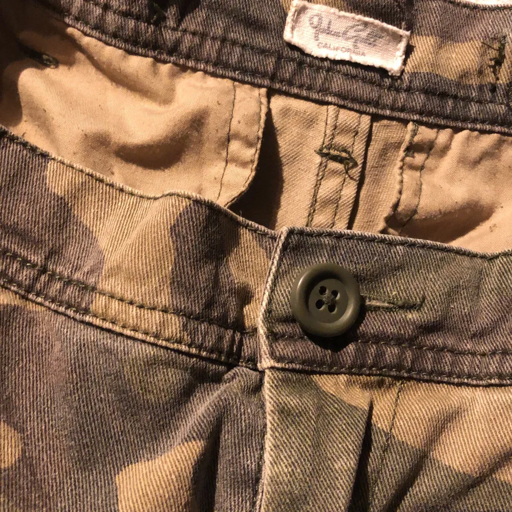 High rise cargo pants. Faded green camo w/ 6 pockets, zip/button closure, belt loops, adjustable waist band detail. 100% cotton. 28cm rise, 76cm in, 71cm waist. Nypris 550kr + frakt. Gently used excellent condition. Item is predistressed. Pet/smoke free. . Jeans & Byxor.