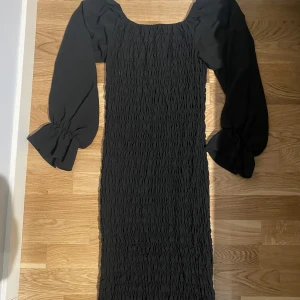 Klänning med volang  - Väldigt fin klänning som formar kroppen till dens bästa form. Fint material som är skönt och ärmar som är synliga. Kan bäras med axlarna på och offshoulder. Kommer ungefär till början av knäna. 