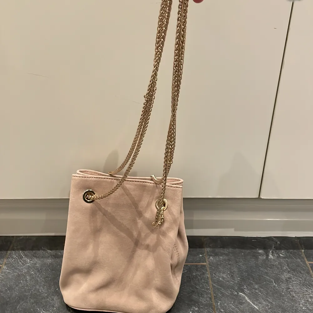 En rosa-Beige väska med guld kedja (ej äkta guld). Den är från H&M och säljs eftersom den aldrig har använts. Den har två fack, ett stort och ett lite mindre på ena sidan av väskan. Finns i centrala Sundbyberg. . Laukut & Käsilaukut.
