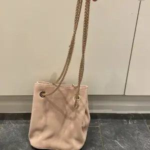 En rosa-Beige väska med guld kedja (ej äkta guld). Den är från H&M och säljs eftersom den aldrig har använts. Den har två fack, ett stort och ett lite mindre på ena sidan av väskan. Finns i centrala Sundbyberg. 