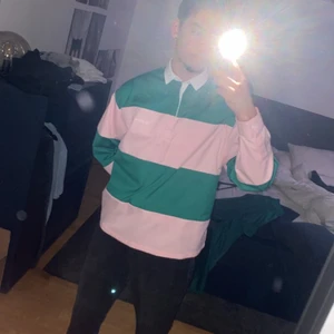 ASOS rugbytröja, oversize - En oversized rugbytröja i ljusrosa och grön färg. Storlek medium (M). En cool tröja som passar dig med lite mer vågad stil och/eller skate samt vintage stil.