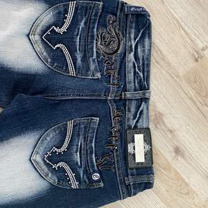 Low waist jeans som bara är testade inomhus från 2000-talet, skitsnygga som är mörkblåa med lightwash på låren och neröver. Fint bling på röven som inte är något fel med. Säljs pga förstora för mej🤍 Står ”crazy h0e” på den lilla silverplattan och på texten över fickorna står de ”dont worry”Finns ett litet hål vid hälen (sista bilden) mått finns!!