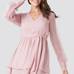 Klänning i ljusrosa  - En fin rosa långärmad klänning i storlek 36 från Paola Marias kollektion med NA-KD. Har tillhörande midjeband och har knappar på slutet av ärmarna. Endast använd en gång på skolavslutning för tre år sedan, säljes för den aldrig används och är nu tyvärr för liten för mig. Eftersom nyskick vill jag ha 270kr-300kr för klänningen, nypris 399kr. Köparen betalar för frakt, annars kan den hämtas upp i Ängelholm.